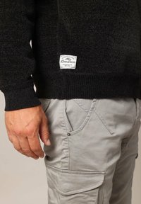 Pull noir texturé avec des poignets côtelés, orné d'une étiquette de marque blanche. Assorti à un pantalon gris clair avec un design de poches diagonales.