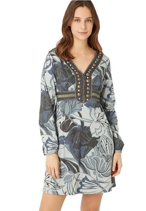 Vestido de manga larga y cuello en V en azul claro con patrones florales en azul oscuro, gris y blanco. Presenta botones decorativos y acentos bordados.