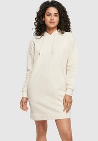 Abito felpa color crema realizzato in tessuto morbido, con vestibilità ampia, maniche lunghe, cappuccio con coulisse e polsini e orlo a costine.