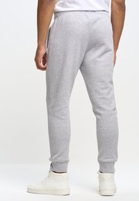 Grå sweatpants med en afslappet pasform, elastisk talje, sidelommer og ribbede afslutninger. Båret med hvide high-top sneakers.