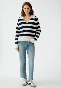 Gestreifter Pullover in Marineblau und Weiß mit V-Ausschnitt und Kragen, kombiniert mit hellblauen Jeans im geraden Schnitt und strukturierten Sneakers.