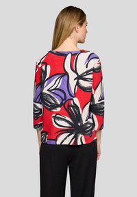 Colorful floral patterned top featuring a red background with black, white, and purple accents; three-quarter sleeves; textured fabric.