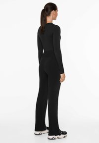 Svart långärmad bodysuit med åtsittande design och hög midja, matchad med svarta utsvängda byxor. Materialet verkar vara mjukt och elastiskt.
