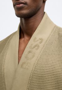 Accappatoio beige con motivo a nido d'ape testurizzato. Il colletto presenta un delicato logo "BOSS" in rilievo lungo il bordo.