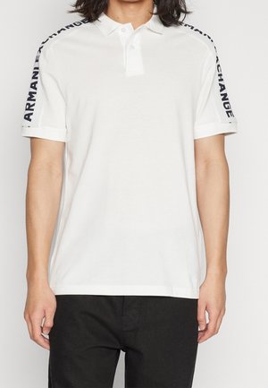 White short-sleeve polo shirt with black "ARMANI EXCHANGE" text on both shoulder stripes, worn with black pants.