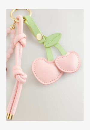 Llavero de cuero rosa que presenta dos cerezas en forma de corazón, acentuadas con hojas verdes y un botón dorado, sujeto a una correa trenzada rosa.