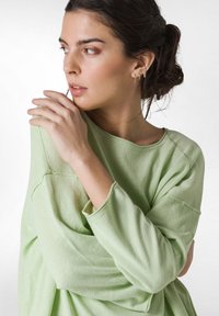 Jasnozielony, oversize'owy sweatshir z okrągłym dekoltem i długimi rękawami. Materiał wydaje się miękki, z widocznymi detalami szwów.