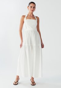 Vestido maxi blanco con escote cuadrado, tirantes halter, pecho fruncido y falda en capas; hecho de una tela ligera con una textura suave.