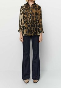 Brązowa i czarna koszula w panterkę z długim rękawem, zestawiona z ciemnymi dzwonami i beżowymi szpilkami.