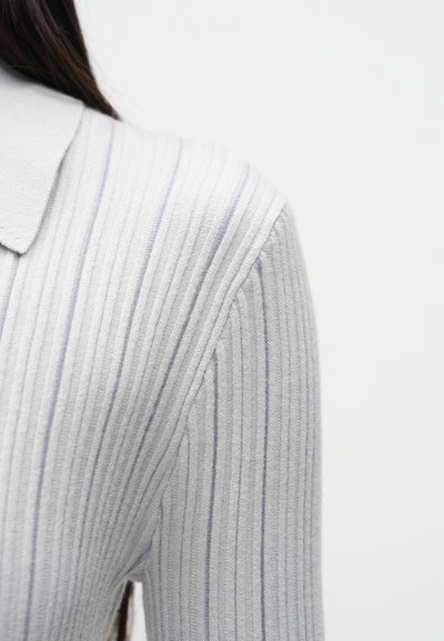 Svetlosivý rebrovaný sveter s jemnými modrými pruhmi. Má klasický golier a textúrovanú tkaninu, ktorá zvýrazňuje jeho priliehavý strih.
