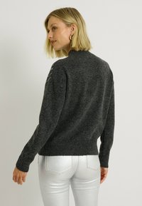 Pull en maille gris foncé avec un col montant et un ourlet côtelé. Présente un motif en maille décoratif sur les épaules et les manches longues.