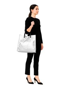 Borsa tote metallizzata argento con manici neri, forma rettangolare grande, texture liscia e senza motivi visibili, tenuta da una persona in abbigliamento nero.