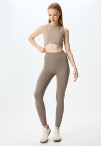 Lichtbruine naadloze crop top en hoge taille leggings, beide gemaakt van een zachte, rekbare stof. Witte sportschoenen maken de outfit compleet.