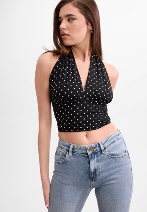 Junge Frau trägt schwarzen Neckholder-Punkte-Crop-Top und hellblaue hoch taillierte Jeans, schaut zur Seite.