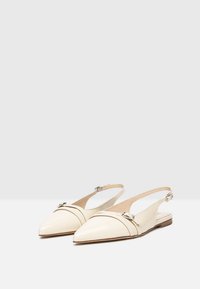 Scarpe slingback in pelle verniciata color crema con punta appuntita, dettagli con cinturino, tacco piatto e fibbie. Finitura esterna liscia.
