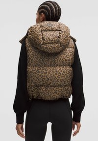 Puffert vest i leopardprint med en stor hætte, brun baggrund og sorte detaljer. Har en quiltet tekstur og en tætsiddende afslutning.