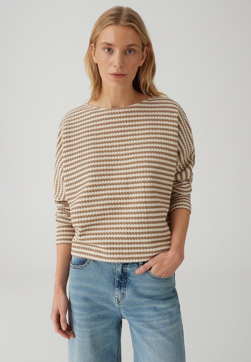 Maglione a righe in beige e bianco; ampia scollatura a barca, spalle scese e vestibilità rilassata. Abbinato a jeans in denim azzurro chiaro.