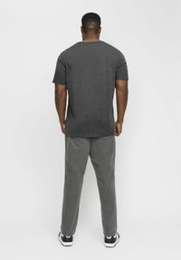 Camiseta de manga corta gris oscuro con escote redondeado, combinada con pantalones gris claro, vista desde la parte de atrás. Zapatillas de deporte en blanco y negro visibles.