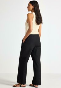 Top in maglia crema con dettagli tridimensionali abbinato a pantaloni neri a gamba larga, con un motivo delicato e tasche laterali. Sandali neri.