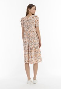 Blumenkleid in Midi-Länge mit Puffärmeln, gemustert mit orangefarbenen, blauen und grünen Blumen auf einem hellpeachfarbenen Hintergrund. Gestufter Rockdesign.