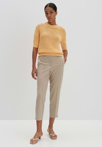 Geel gebreid kort mouwtrui, beige taps toelopende broek en zwarte instap sandaaltjes. Glad oppervlak, ontspannen pasvorm en casual ontwerp.