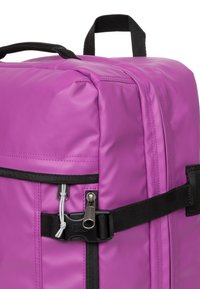 Purpurowy plecak nylonowy z czarnymi akcentami, wyposażony w uchwyt u góry, zamek błyskawiczny i regulowane paski. Gładka tekstura z detalami w szwach.