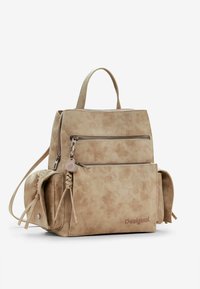 Sac à dos en simili cuir beige avec plusieurs compartiments zippés, surface texturée, accents tressés et une poignée supérieure. Nom de la marque embossé.