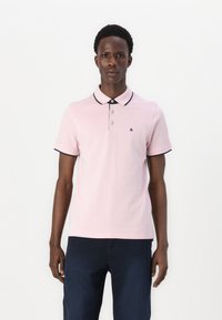 Roze polo shirt met zwarte afwerking op de kraag en mouwen, voorzien van drie knopen en een klein logo op de linkerborst.