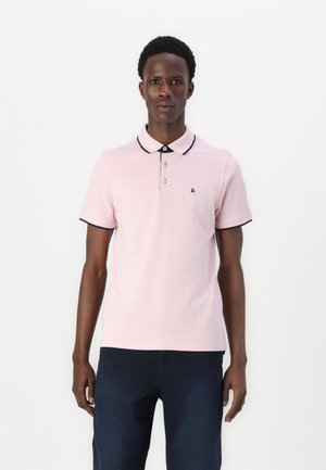 Roze polo majica s crnim obrubom na ovratniku i rukavima, s tri gumba i malim logotipom na lijevoj strani prsnog dijela.