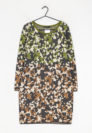 Robe à manches longues avec un motif camouflage abstrait vert, marron et gris foncé sur fond beige, suspendue à un cintre noir.