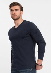 Camisa de manga larga azul marino con cuello en V en una tela suave, con un diseño ajustado y costuras minimalistas, combinada con unos pantalones vaqueros azules informales.