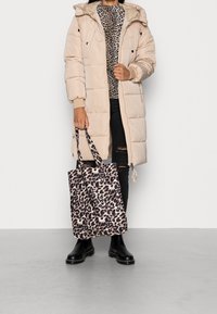 Beige pufferjakke med hætte, der har to forlommer. Sort leopardmønstret totebag, parret med sorte ripped jeans og sorte ankelstøvler.