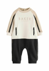 Ensemble pour tout-petit composé de deux pièces : un haut crème avec un logo et des accents beiges, associé à un pantalon noir. Comprend des poches zippées et des pressions.