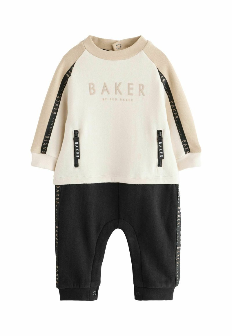 Ensemble pour tout-petit composé de deux pièces : un haut crème avec un logo et des accents beiges, associé à un pantalon noir. Comprend des poches zippées et des pressions.