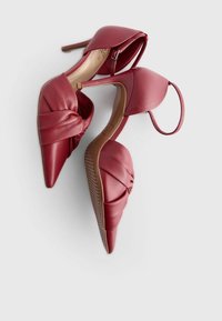 Chaussures à talons hauts en cuir rouge avec un bout pointu et un design noué sur le devant. Bride de cheville réglable et semelle texturée.