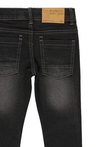 Vaqueros de denim negro con un corte entallado, que presentan una etiqueta de cuero marrón, dos bolsillos traseros y costuras contrastadas.