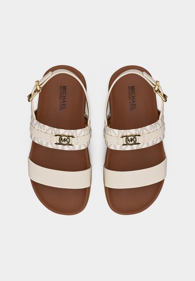 Γυναικεία φλατ σανδάλια με καφέ πάτους, κρεμ λουράκια, ρυθμιζόμενες αγκράφες και λογότυπο Michael Kors στα διακοσμημένα λουράκια.