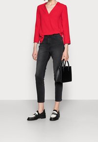 Blusa rossa a V, jeans skinny scuri, scarpe slip-on bianco e nere, borsa nera. Tessuto morbido e vestibilità sagomata.