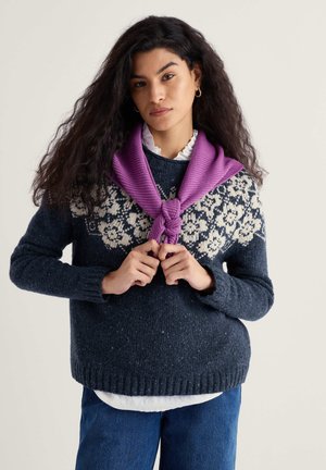 Marineblauer Strickpullover mit weißen Blumenmustern auf der Brust, getragen über einem weißen Hemd mit Kragen, und einem gedrehten lila Schal um den Hals.