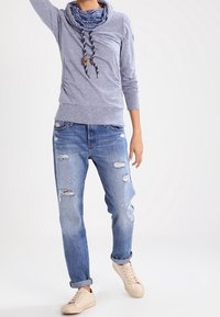 Hellgrauer Pullover mit einem Schalkragen und Kordeln. Tragen mit verwaschenen blauen Jeans und beigen Turnschuhen. Lässig, entspannte Passform.