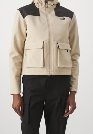 Beige en zwarte North Face jas met rits aan de voorkant, klepzakken op de borst, gedragen met zwarte cargobroek met zakken.