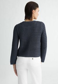 Navyblauwe gestructureerde trui met een boxy fit, lange mouwen en een geribbelde zoom. Gecombineerd met witte hoge taillebroeken.