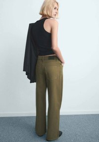 Pantalones de pierna ancha de color verde oliva con una textura suave y bolsillos traseros, combinados con una camiseta sin mangas negra y un blazer negro drapeado.