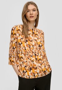 Geprinte top met driekwartmouwen, uitgevoerd in een mix van oranje, bruin en beige kleuren in een gestructureerde stof. Ronde halslijn.