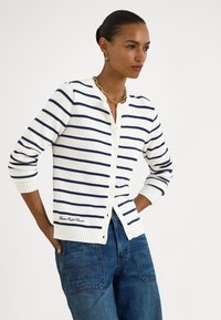 Λευκό ζακετάκι με ναυτικές ρίγες, ριμπ μανσέτες και γιακά. Διαθέτει κλείσιμο με κουμπιά και κεντητό λογότυπο στο τελείωμα. Φοριέται πάνω από τζιν παντελόνια.