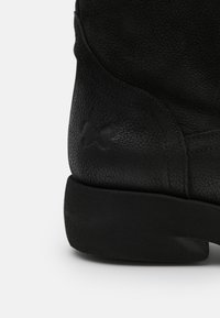 Botte en cuir noir avec une finition texturée, dessus incurvé et semelle plate solide. Design simple avec un logo embossé discret sur le côté.