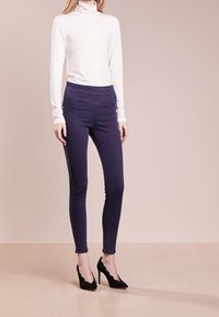 Mörkblå smala jeans med medelhög midja och subtila sömmar på fickorna, kombinerat med en vit långärmad polotröja och svarta klackar.