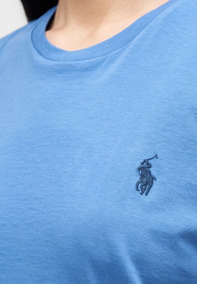 Világoskék pamut póló kerek nyakkal és rövid ujjakkal. A mellrészen egy kis sötétkék hímzett logó található. Puha tapintású.