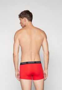 Boxers rouges avec une ceinture noire portant le nom de la marque. Tissu lisse et design ajusté pour le confort et le soutien.