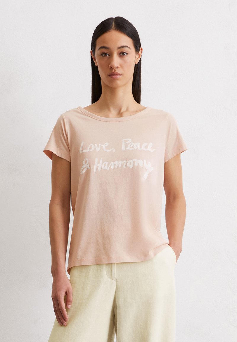 Lichtroze t-shirt van zachte katoen met witte tekst: "Liefde, Vrede & Harmonie." Korte mouwen en een ontspannen, ronde halslijn.